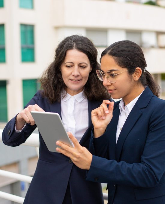 Content businesswomen using tablet pc. Cheerful focused female colleagues standing with digital tablet on urban city street. Wireless technology concept
