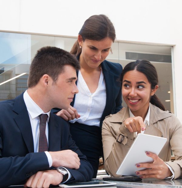 Smiling young woman showing tablet screen to business people. Business man and women discussing issues, standing and sitting at cafe table. Partnership concept. Front view.